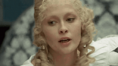 Blonde Curly Hair Woman In White Dress Sitting On Couch GIF