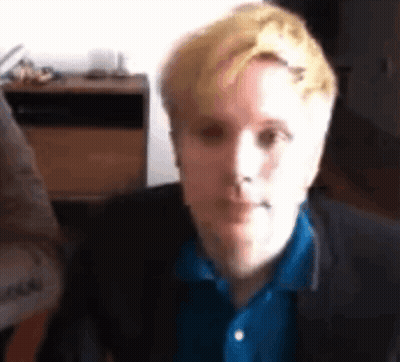 Blonde Man In Blue Shirt And Black Jacket Looking At Camera GIF