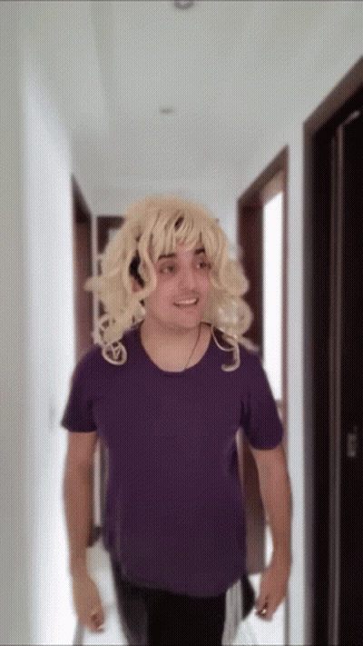 Blonde Wig Man In Purple Shirt Walking Down Hallway GIF