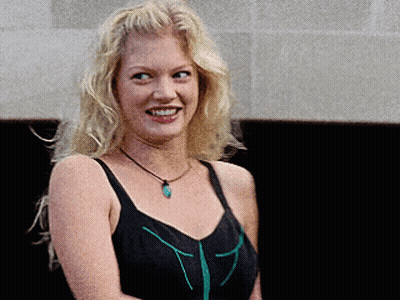 Blonde Woman In Black Tank Top And Green Necklace Smiling GIF