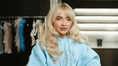 Blonde Woman In Blue Hoodie Among Clothes Racks GIF