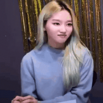 Blonde Woman In Blue Sweater Before Gold Curtain GIF