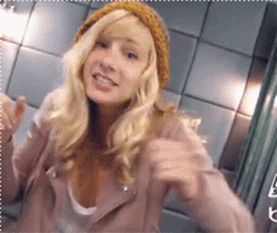 Blonde Woman In Pink Jacket And Yellow Beanie Pointing GIF