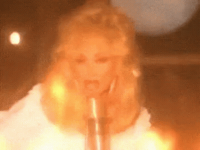 Blonde Woman Singing Into Microphone In Front Of Fire GIF