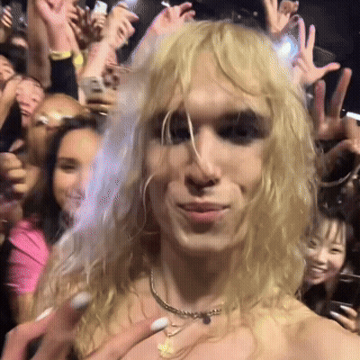 Blonde Woman With Gold Necklace In Front Of Crowd GIF