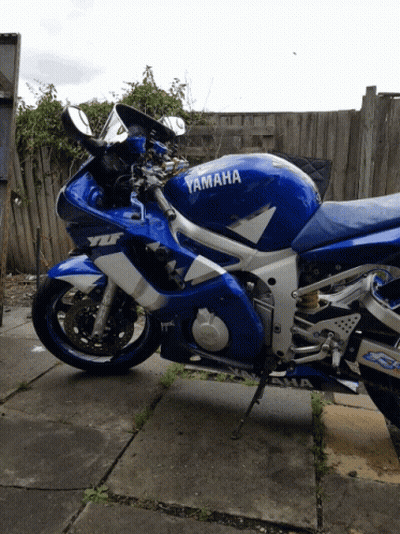 Blue And White Yamaha Motorcycle Parked In Front Of Fence GIF