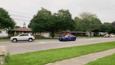 Blue Car Driving Down Street Next To White SUV And House GIF