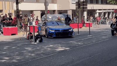 Blue Car Driving Down Street With Crowd GIF