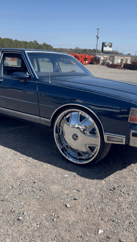 Blue Car With Chrome Wheels Parked On Gravel GIF