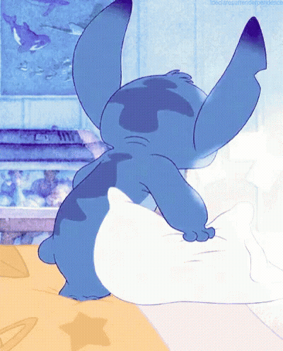 Blue Cartoon Character Laying On Bed With White Pillow GIF