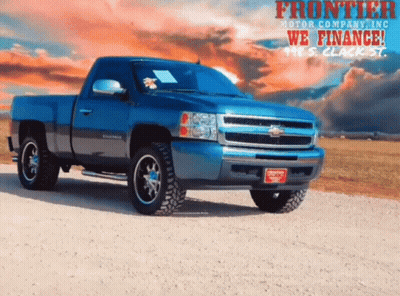Blue Truck Parked On Dirt Road In Front Of Frontier Motor Company Ad GIF
