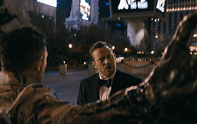 Blurry Man In Tuxedo Walking Past Sign Saying A GIF