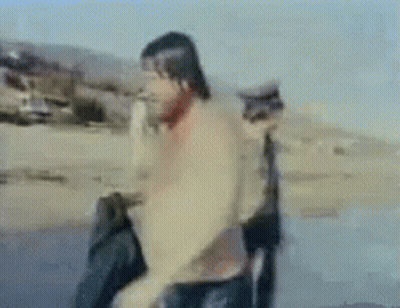 Blurry Man On Beach With Cat Behind Him GIF