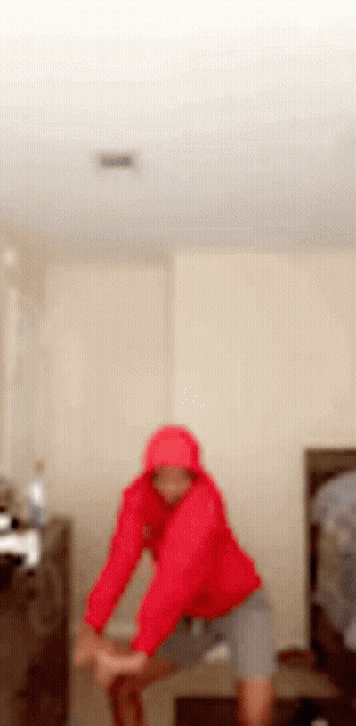 Blurry Person In Red Hoodie Stretching In Bedroom GIF