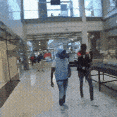 Blurry Picture Of People Walking In Mall With Sign Saying A GIF