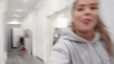 Blurry Woman In Gray Hoodie Standing In Hallway GIF