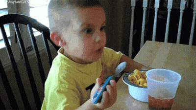 Boy Eating Macaroni And Cheese Holding Remote GIF