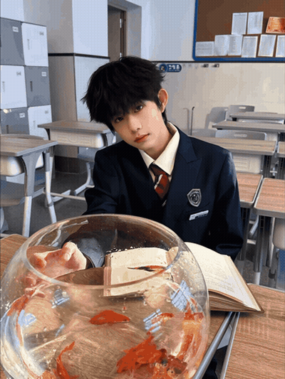 Boy in School Uniform at Desk With Book and Fish Bowl