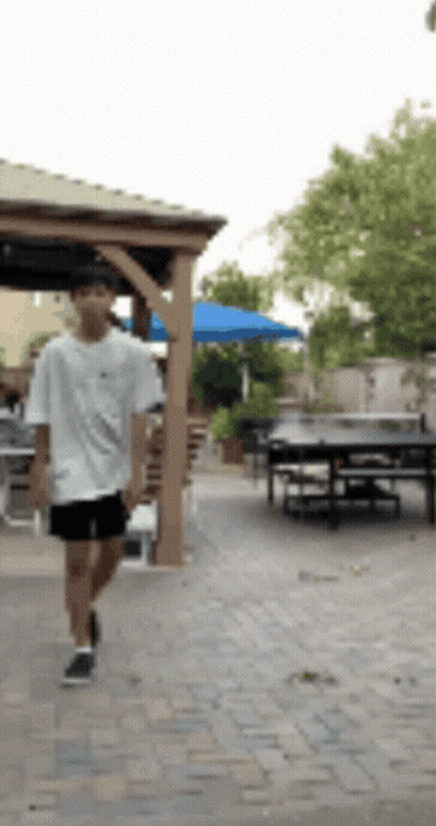 Boy In White Shirt And Black Shorts Walking On Brick Walkway GIF
