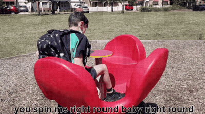Boy Sitting On Red Flower Merry Go Round GIF