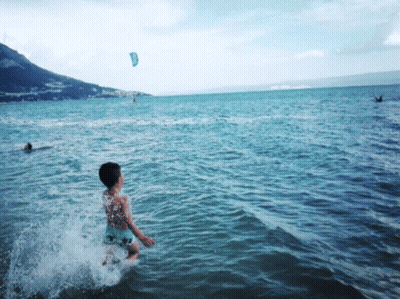 Boy Splashing In Ocean With Kite GIF