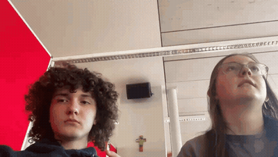 Boy With Curly Hair And Girl With Glasses Standing By Cross GIF