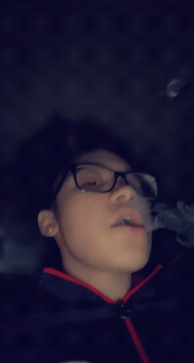 Boy With Glasses Smoking Cigarette In Dark Room GIF