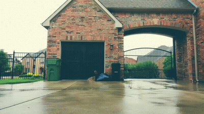 Brick House With Green And Black Trash Cans GIF