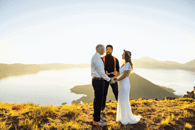 Bride and Groom Holding Hands on Hill Overlooking Lake