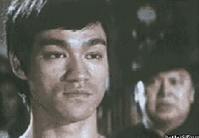 Bruce Lee Looking At Camera, Man In Police Hat Behind GIF