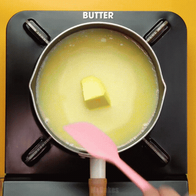 Butter Is Being Stirred In A Pot With A Pink Spatula GIF