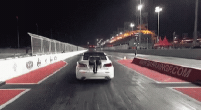 Car Driving Down Race Track At Night With Person Standing On Back GIF