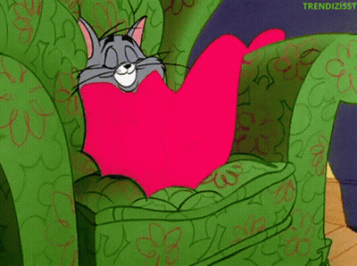 Cartoon Cat Sitting In Green Chair With Pink Heart Pillow GIF