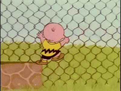 Charlie Brown Is Standing Behind A Chain Link Fence In A Cartoon . GIF