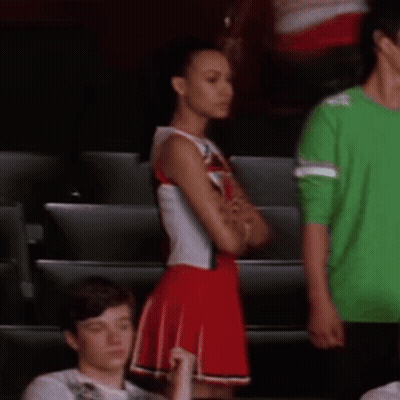 Cheerleader In Red And White Uniform Next To Man In Green Shirt GIF