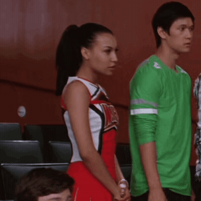 Cheerleader In Red And White Uniform With WMHS Beside Man In Green Shirt GIF