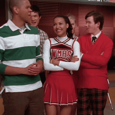 Cheerleader In WMHS Uniform Smiling Beside Man In Green And White Striped Shirt GIF