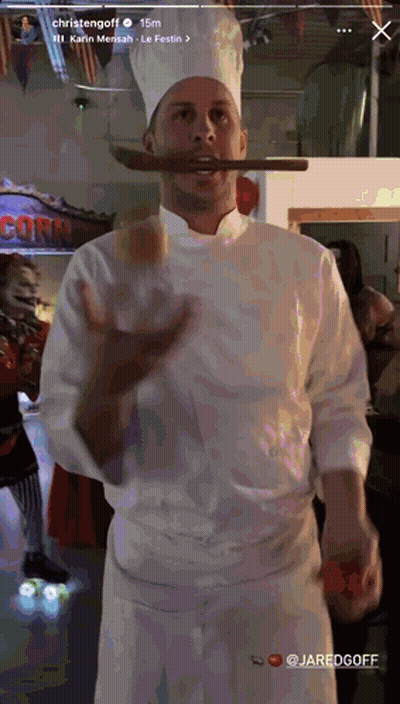 Chef Holding Sausage in Mouth in Front of Corn Sign