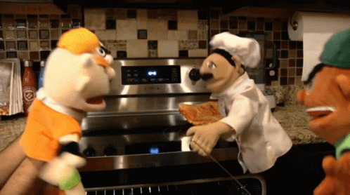 Chef Puppet Holding Pizza In Front Of Stove GIF