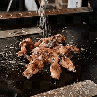 Chicken Wings Are Being Sprinkled With Salt On A Griddle GIF