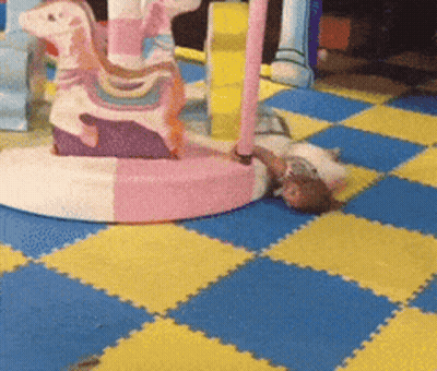 Child Laying On Checkered Floor Beside Pink Horse GIF