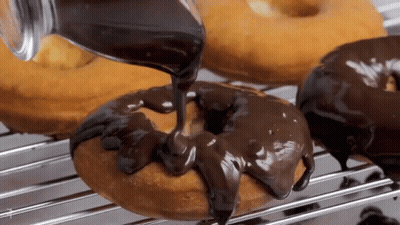 Chocolate Icing Is Being Poured On A Donut On A Rack . GIF