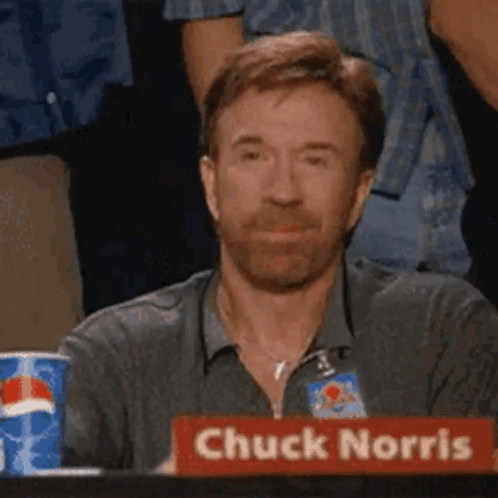 Chuck Norris Is Sitting At A Table With A Red Sign That Says Chuck Norris . GIF