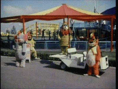 Clowns Standing In Front Of Carousel And Small Car GIF