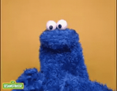 Cookie Monster From Sesame Street Is Standing In Front Of A Yellow Wall . GIF