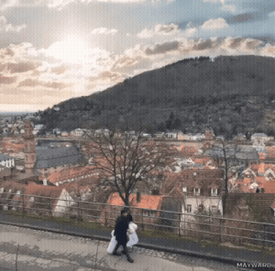Couple Walking On Sidewalk With Mountain And Maywand GIF