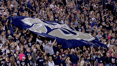 Crowd Holding Blue And White Flag With Letter U GIF