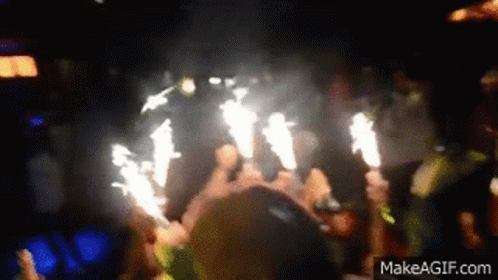 Crowd Holding Sparklers In Dark Room GIF