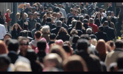 Crowd Walking Down Street With Sign GIF