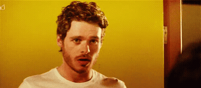 Curly Bearded Man In White Shirt Before Yellow Wall GIF